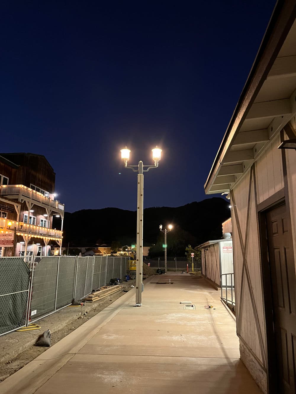 Illuminated streetlamp along pathway at night with mountains in the background.