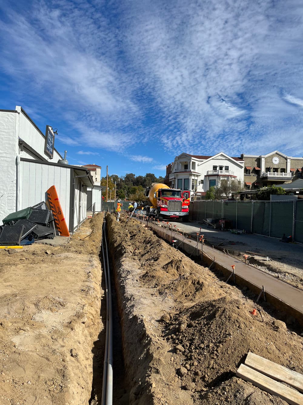 Construction site with a trench and cement truck under a blue sky.