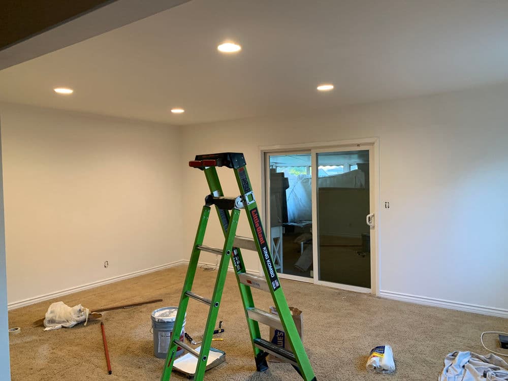 Renovated living room with fresh paint, a ladder, and recessed lighting fixtures.