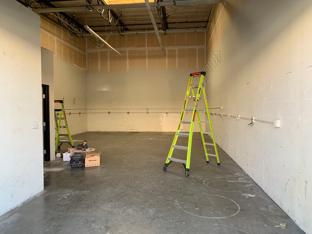 Empty industrial space with two green ladders and construction tools scattered on the floor.