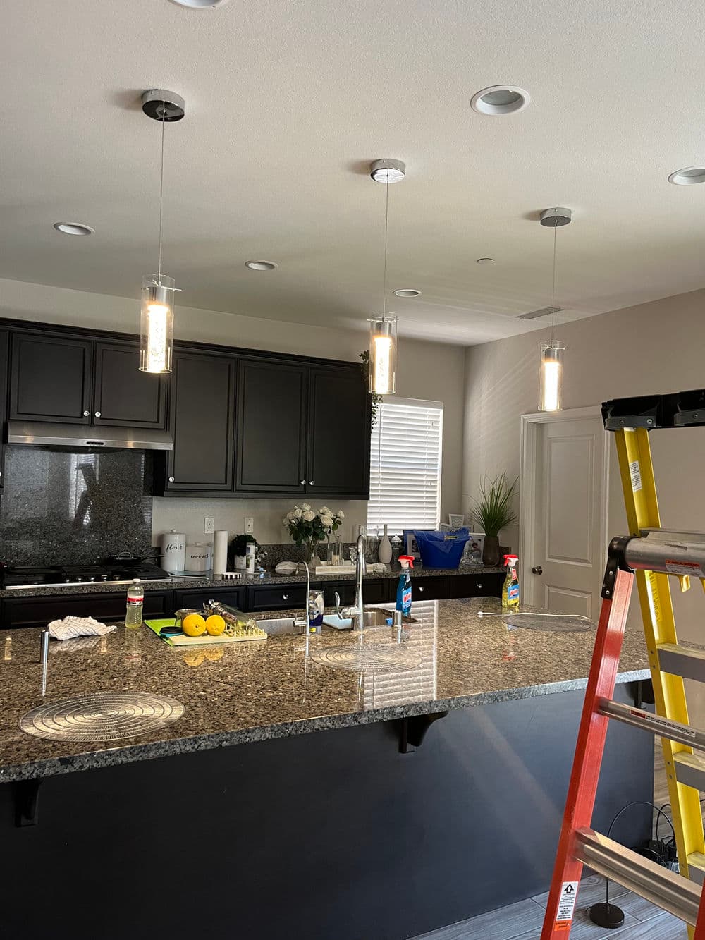 Modern kitchen with black cabinets, granite countertop, and pendant lights over an unfinished island.