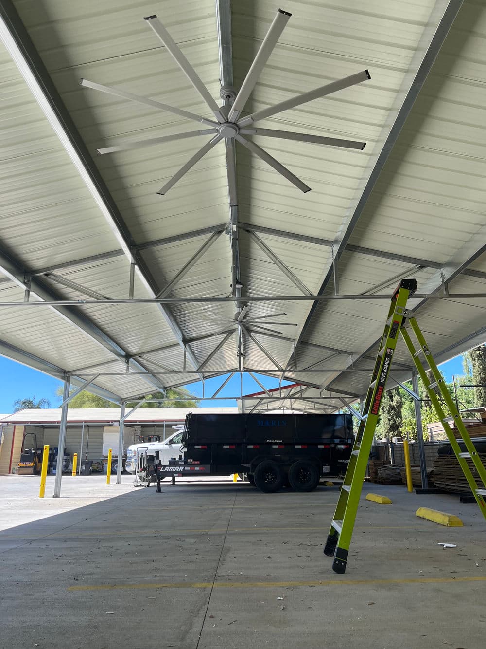 Large indoor space with a fan, ladder, and a truck parked under a metal roof.