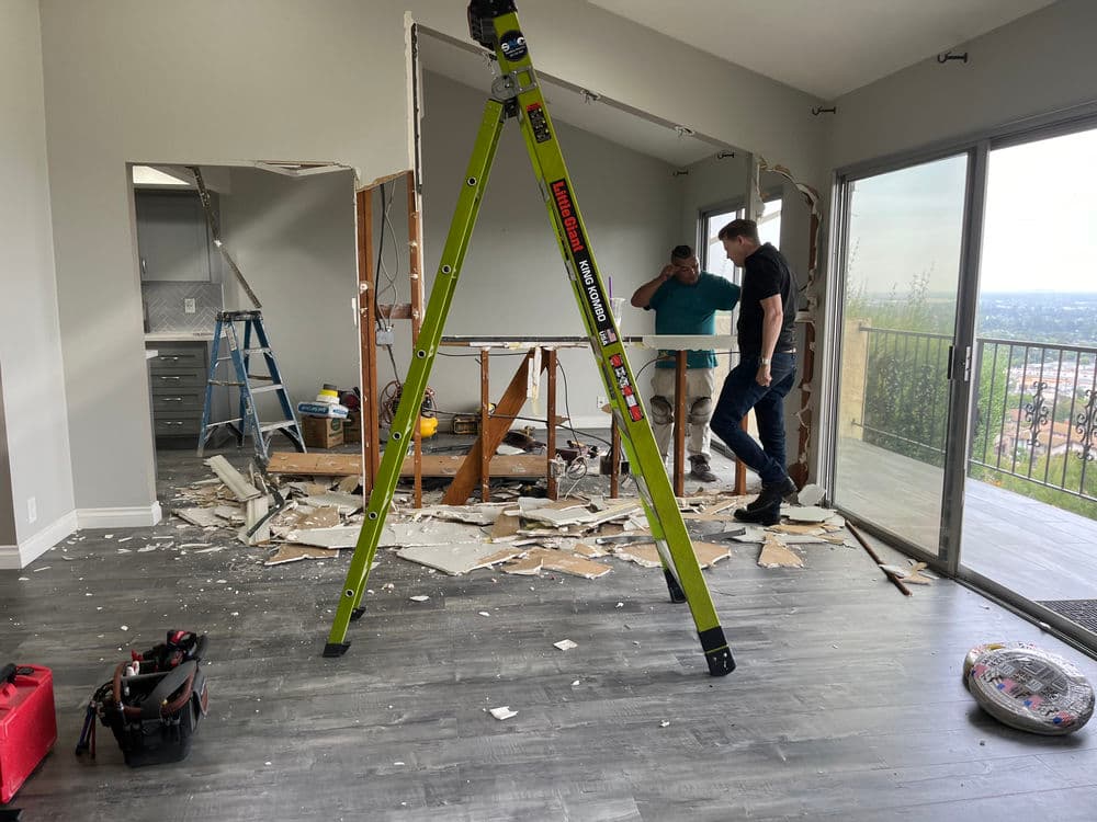 Men renovating a room with debris, ladder, and tools visible, showcasing home improvement progress.