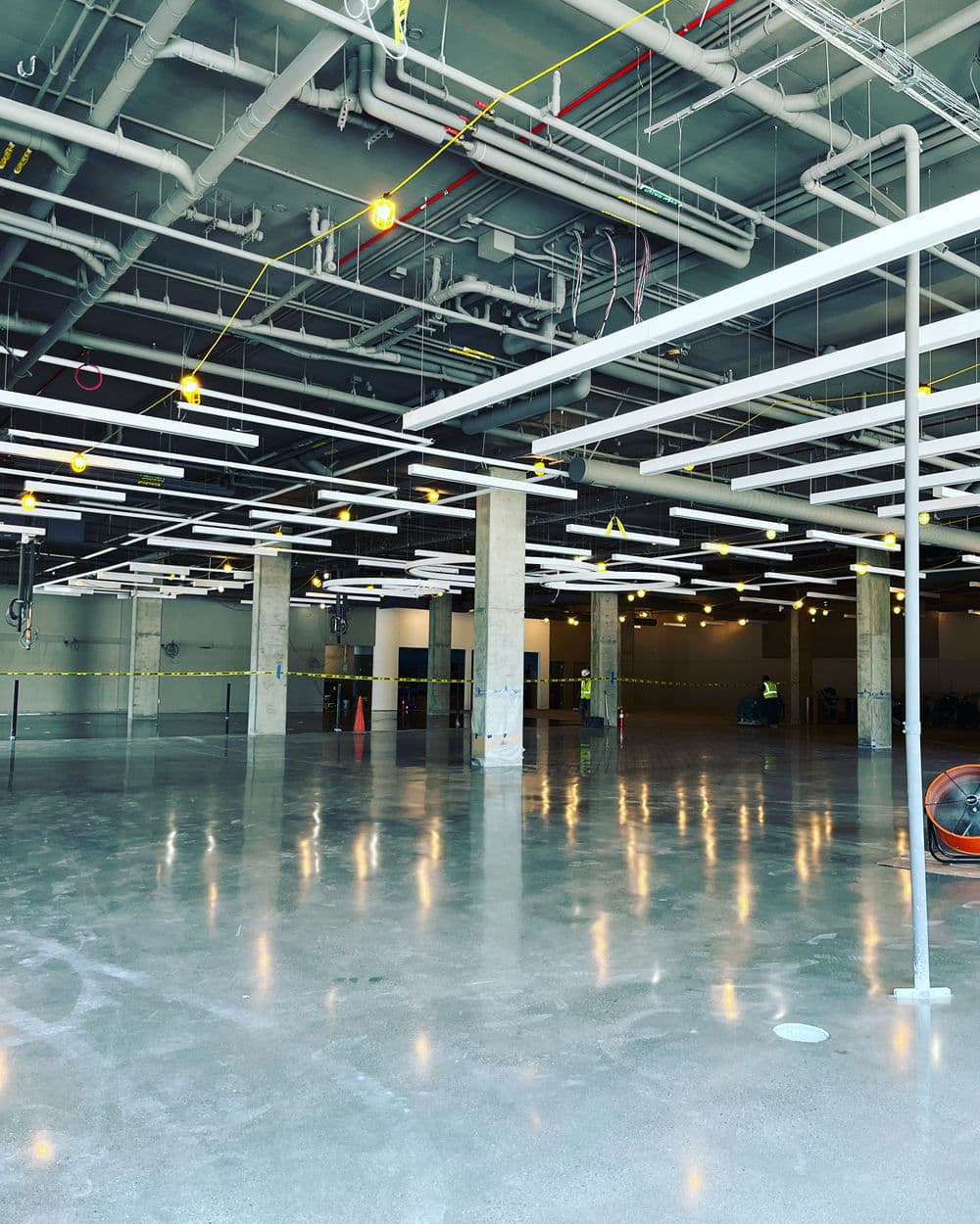Industrial interior of an empty commercial space with exposed pipes and lighting fixtures.