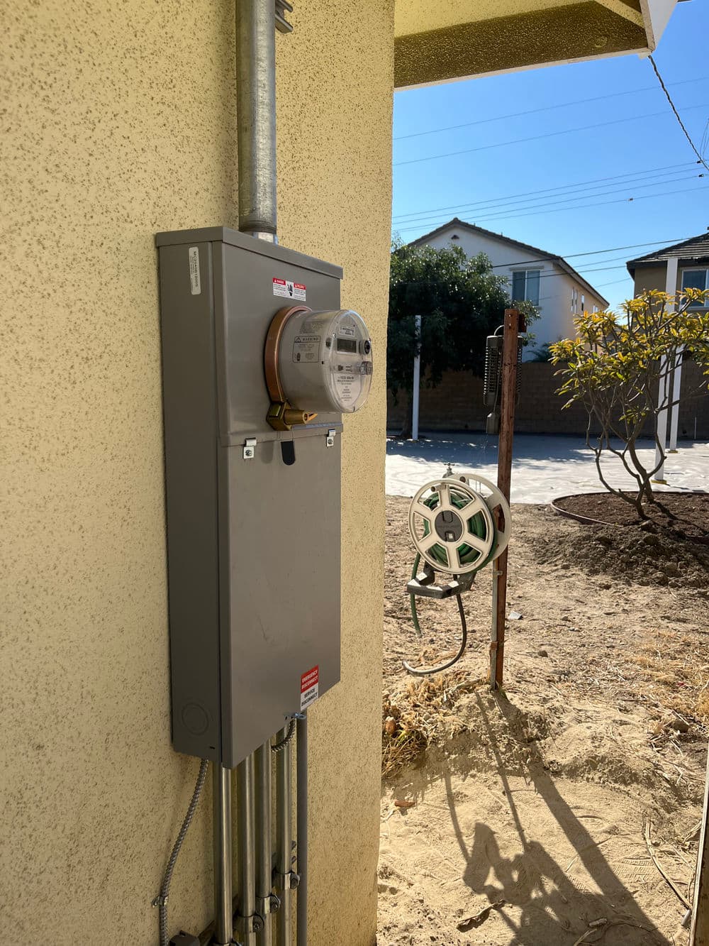 Electric meter mounted on a wall next to a retractable hose reel in a residential area.