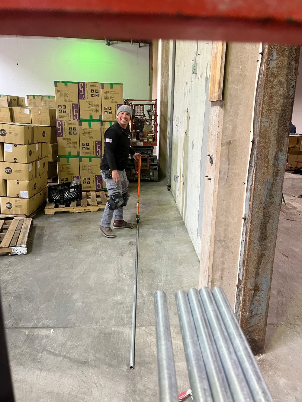 Worker using a tool in a warehouse filled with boxes and stacked materials.