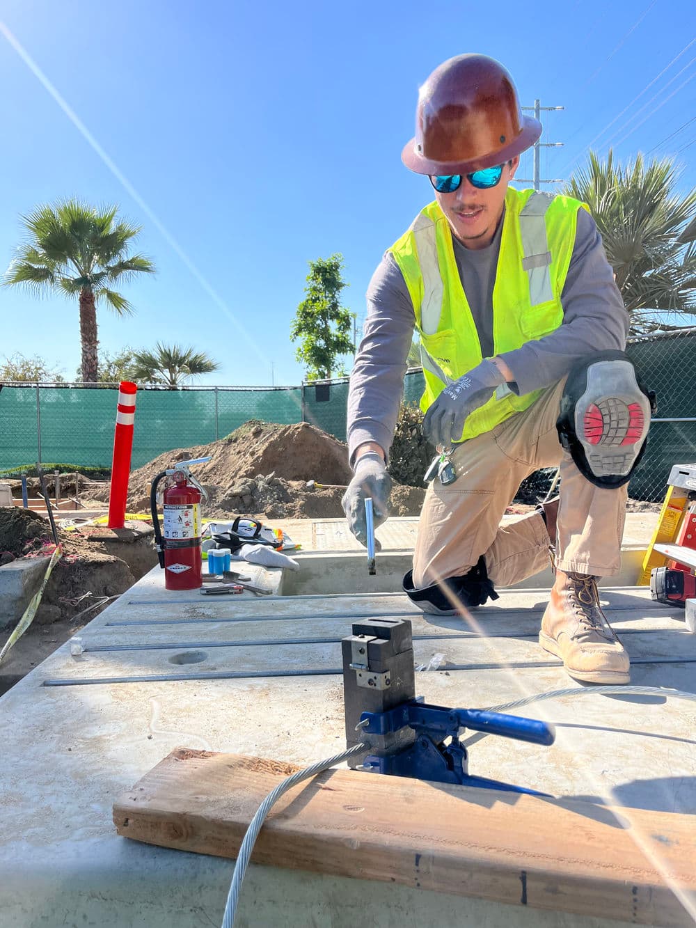 Construction worker in safety gear using tools on a site under clear blue skies.