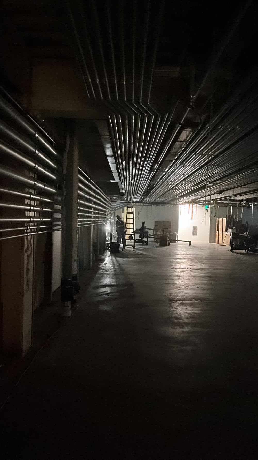 dimly lit underground parking garage with exposed pipes and workers in the distance