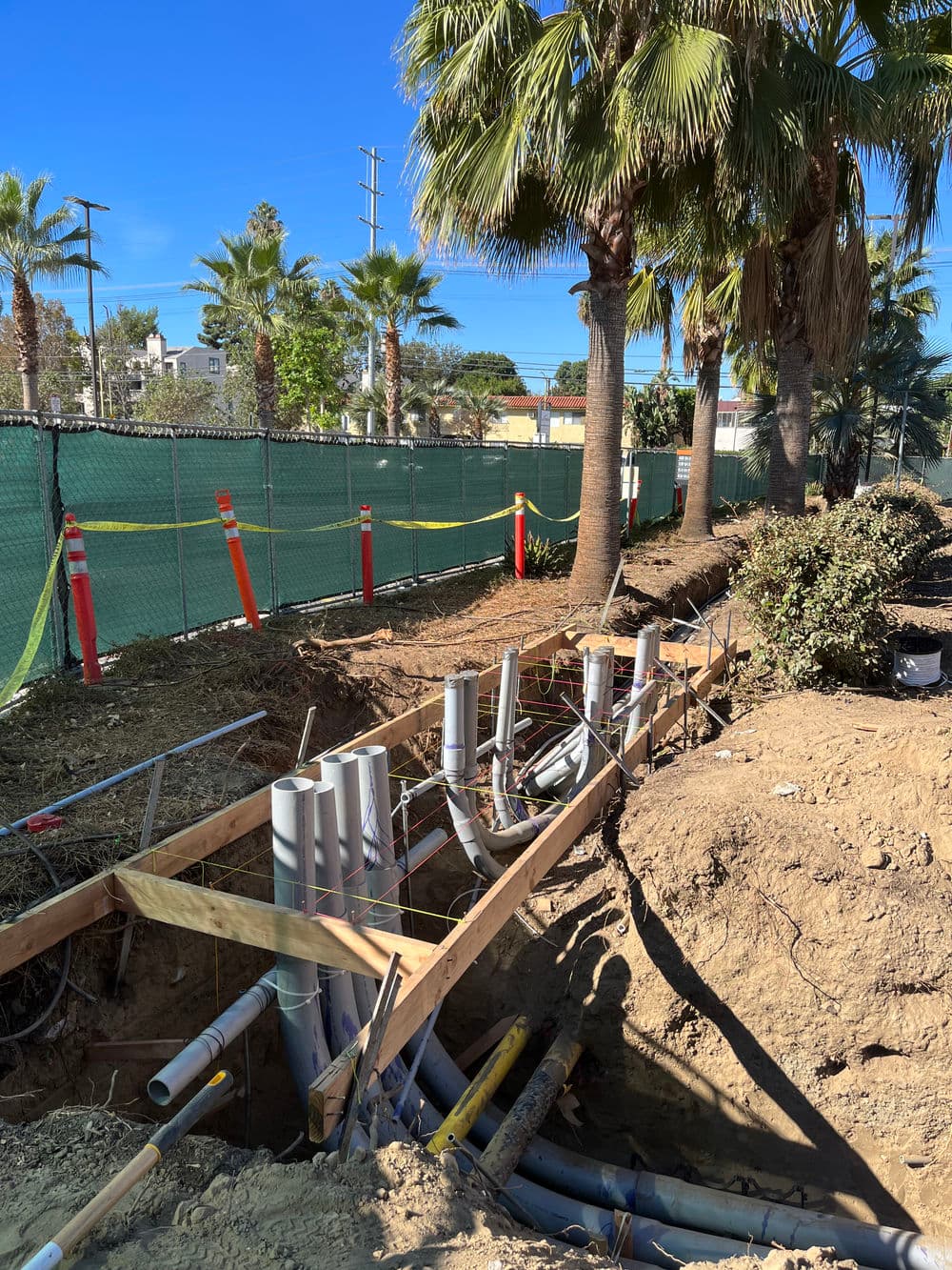 Construction site with exposed drainage pipes and palm trees under a clear blue sky.