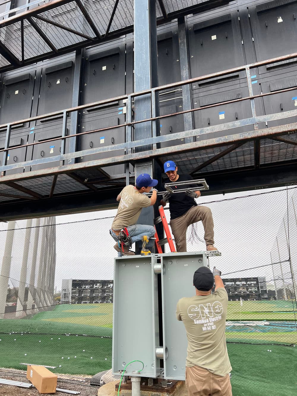 Workers installing equipment on a metal structure at a sports facility, enhancing infrastructure.