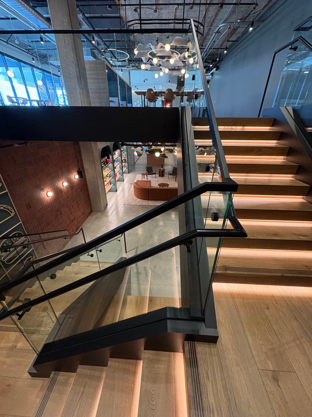 Modern office interior featuring stylish staircase, glass railing, and open workspaces.