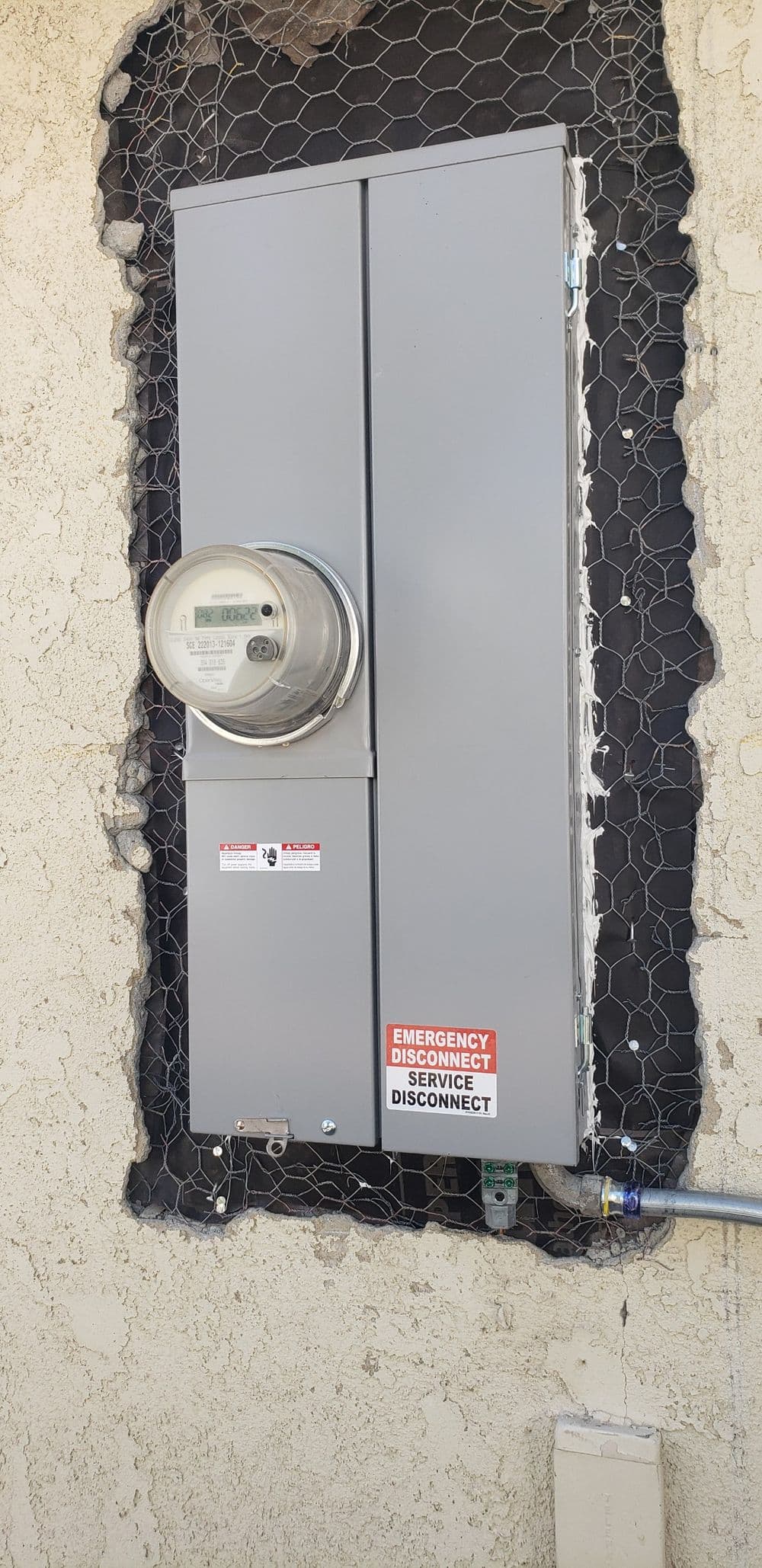 Electric meter box with emergency disconnect label on a textured wall.