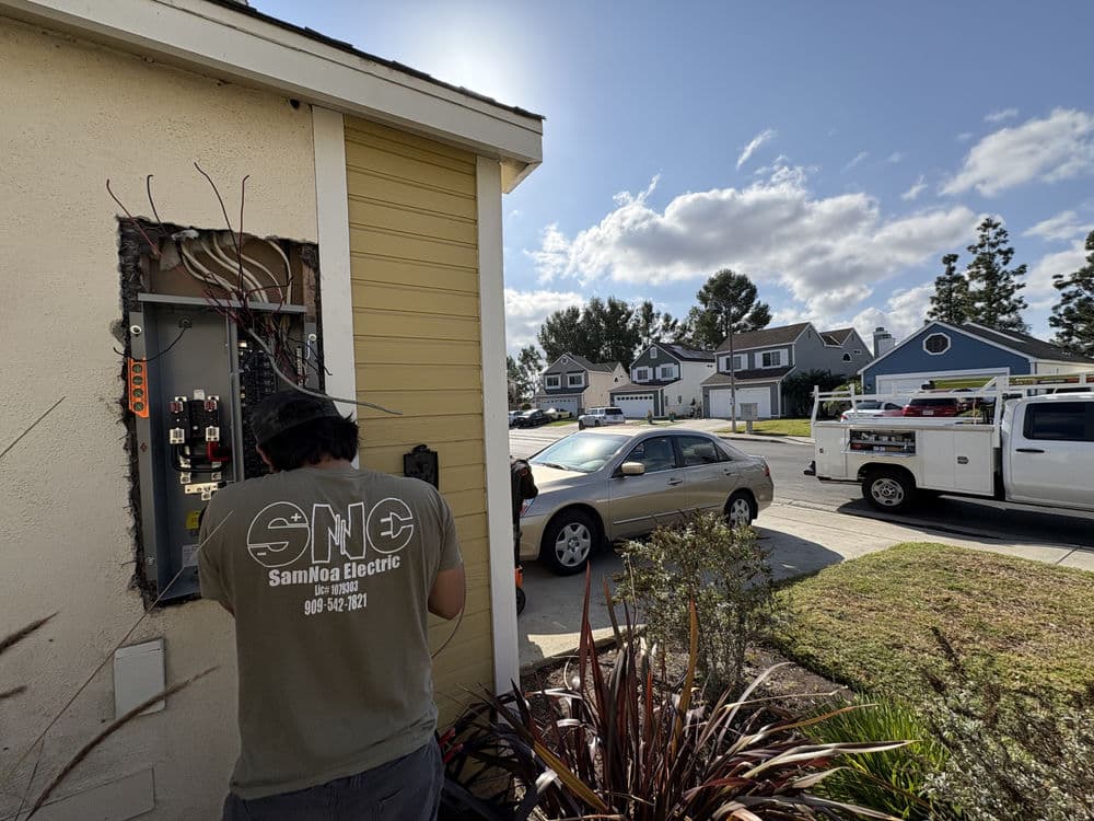 Electrician troubleshooting electrical panel outside a residential home in bright daylight.