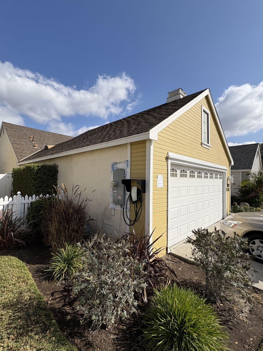 Yellow house exterior with garage, electric vehicle charger, and well-maintained landscaping.