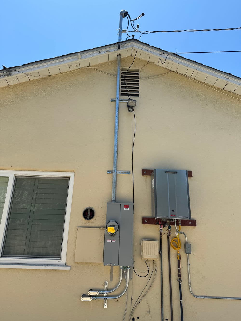 Electrical installation on exterior wall featuring meter box and conduits against light background.