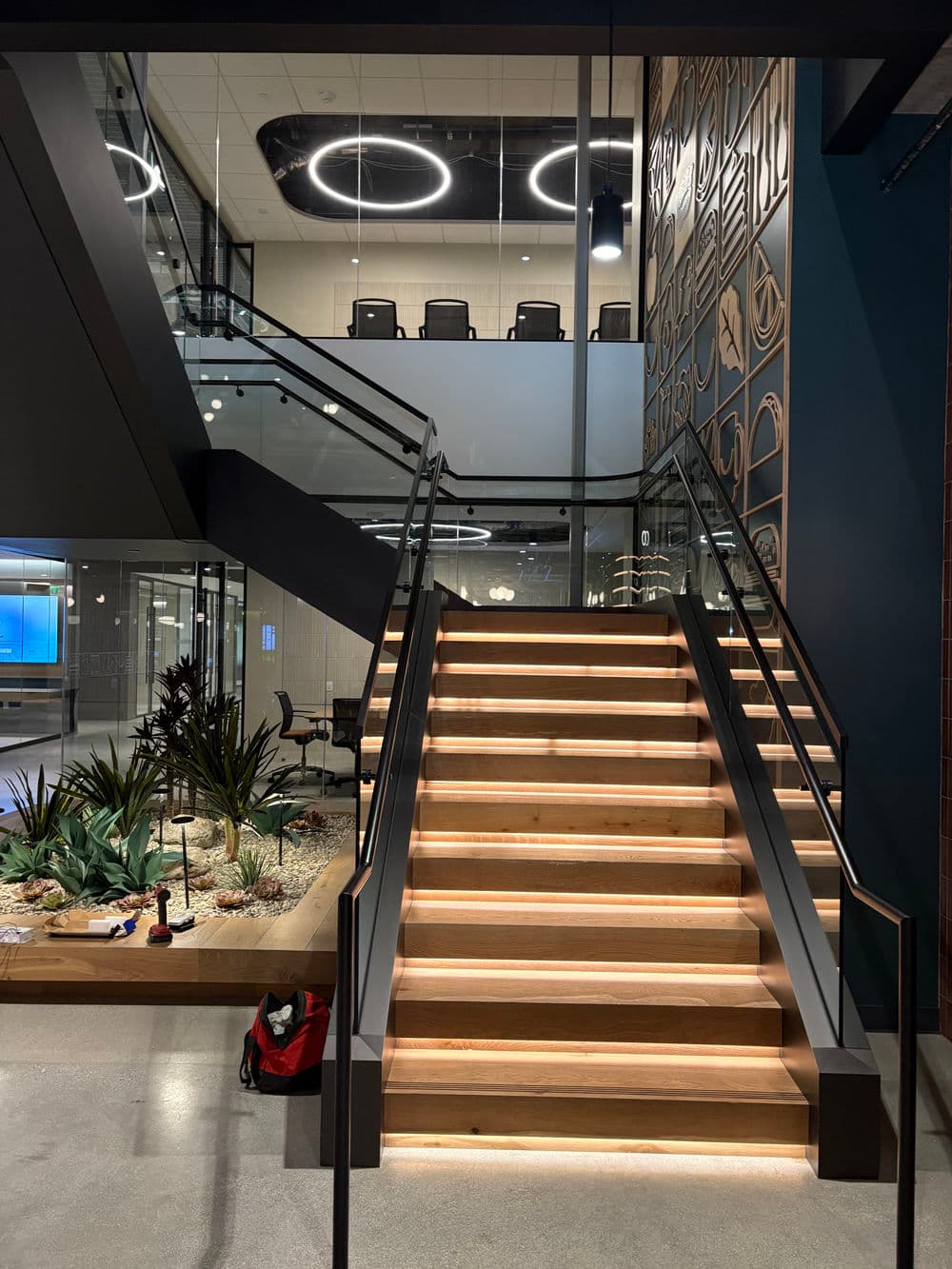 Modern office interior with illuminated wooden stairs leading to a glass-enclosed upper level.