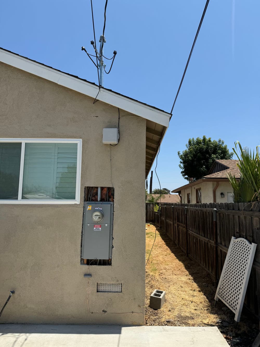 Side view of a house showing an electrical meter, power lines, and a clear blue sky.