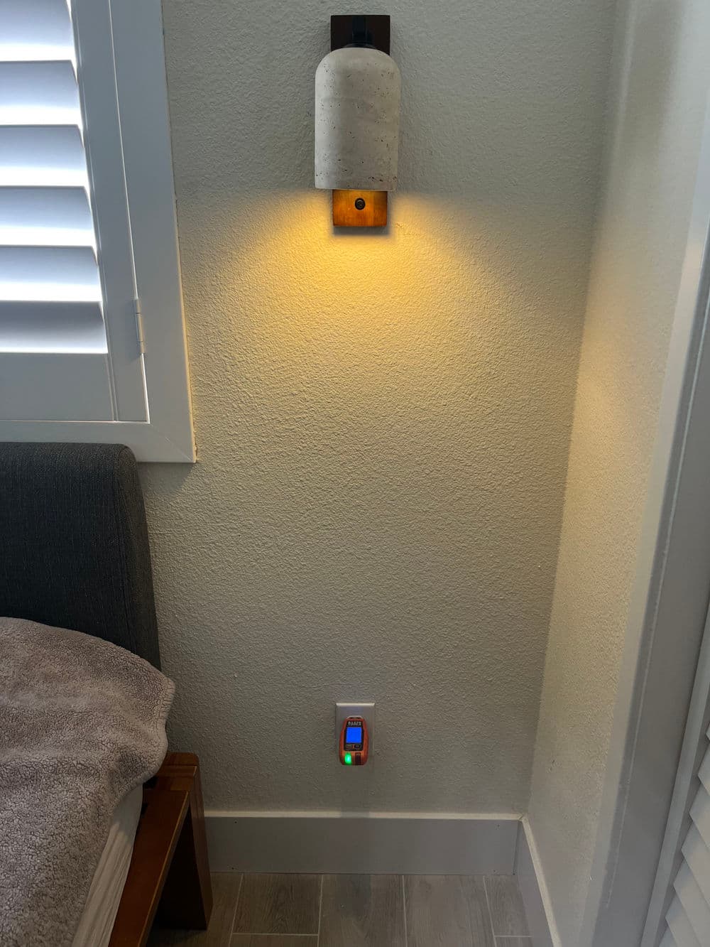 Modern wall lamp illuminating a cozy corner with a colorful smart plug by a bed.