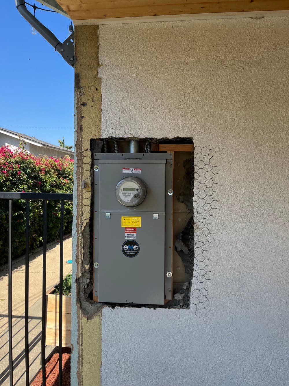 Electric meter mounted on wall with exposed wiring and surrounding construction details.