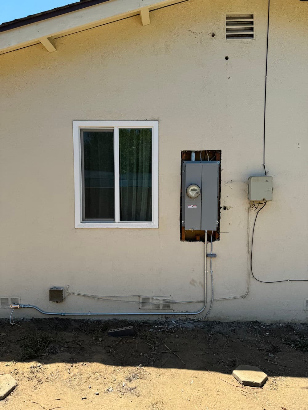 Electric meter installation on exterior wall next to window, with wiring visible.