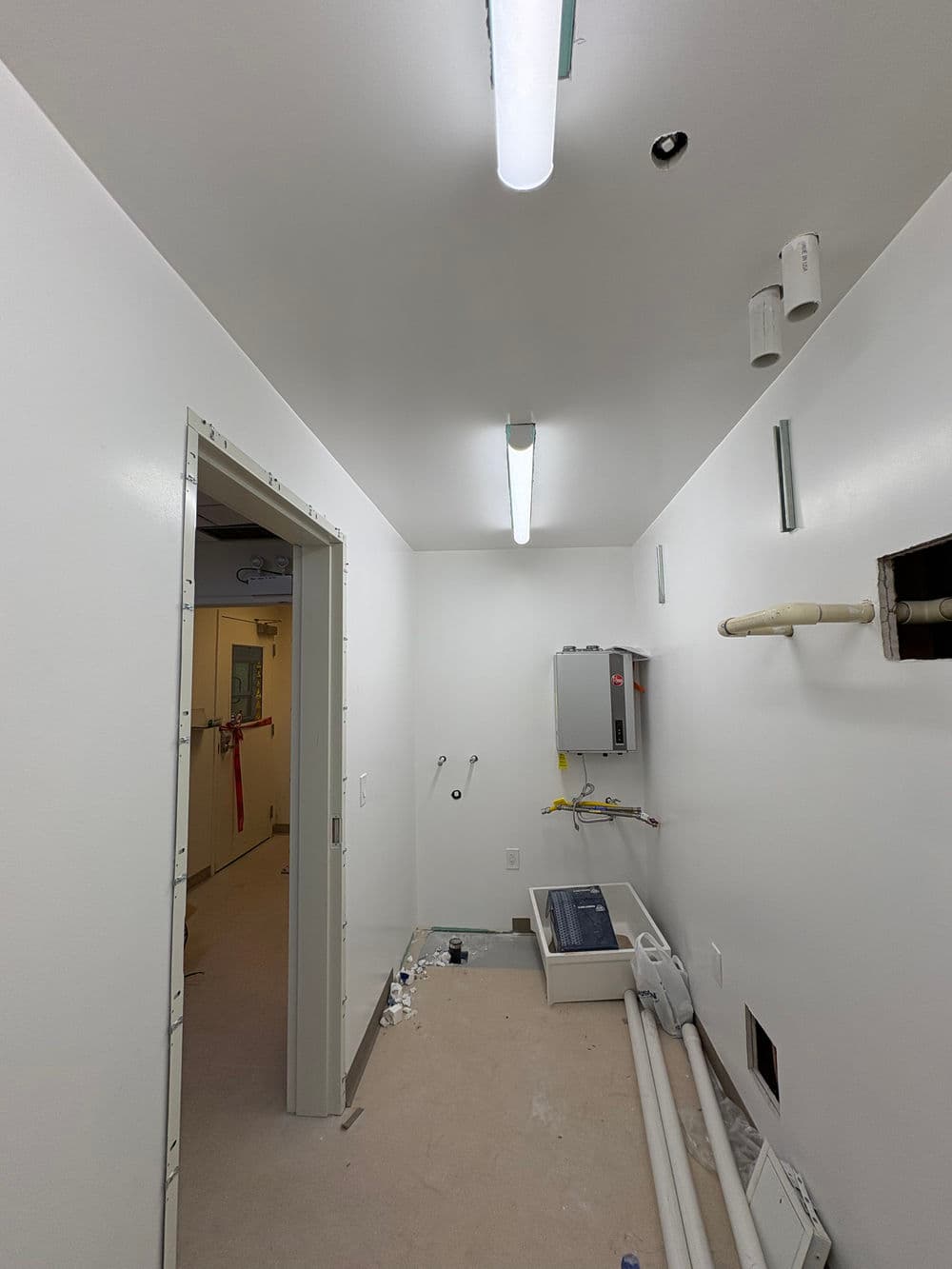 Empty interior of a commercial utility room with fluorescent lighting and plumbing fixtures.