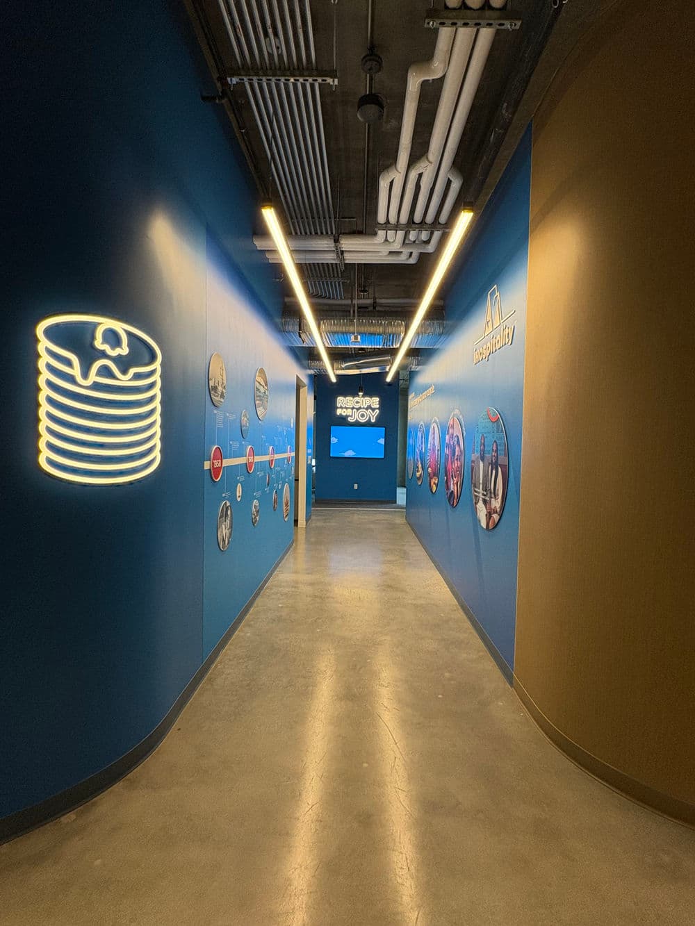 Modern hallway with blue walls featuring neon pancake sign and photo displays.