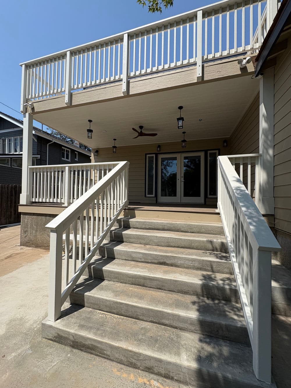 Modern home exterior with a spacious deck, white railings, and concrete stairs.