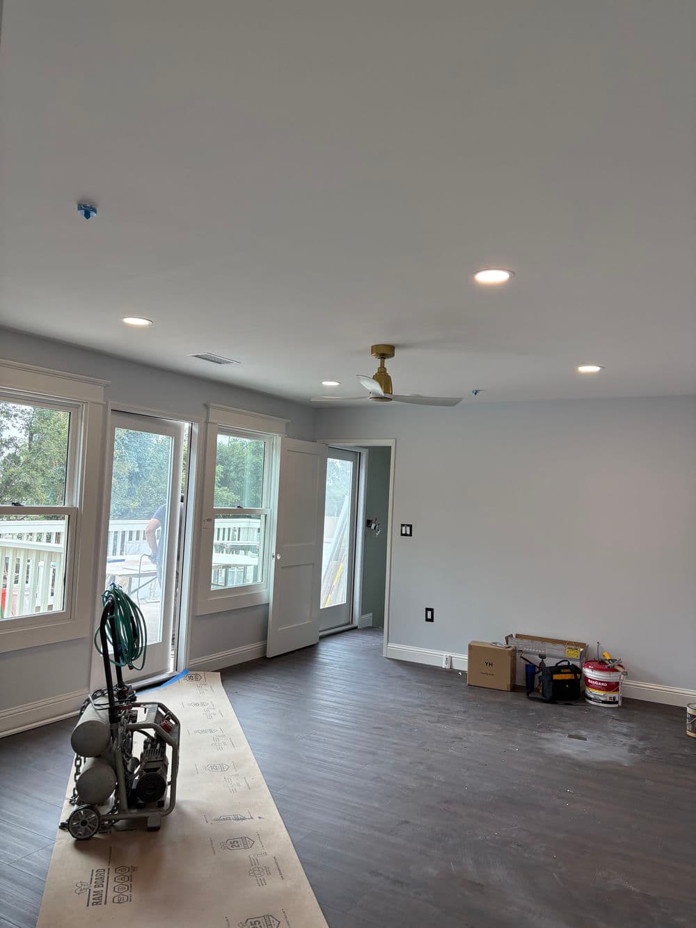 Bright interior room with new ceiling fan, large windows, and light wood flooring.