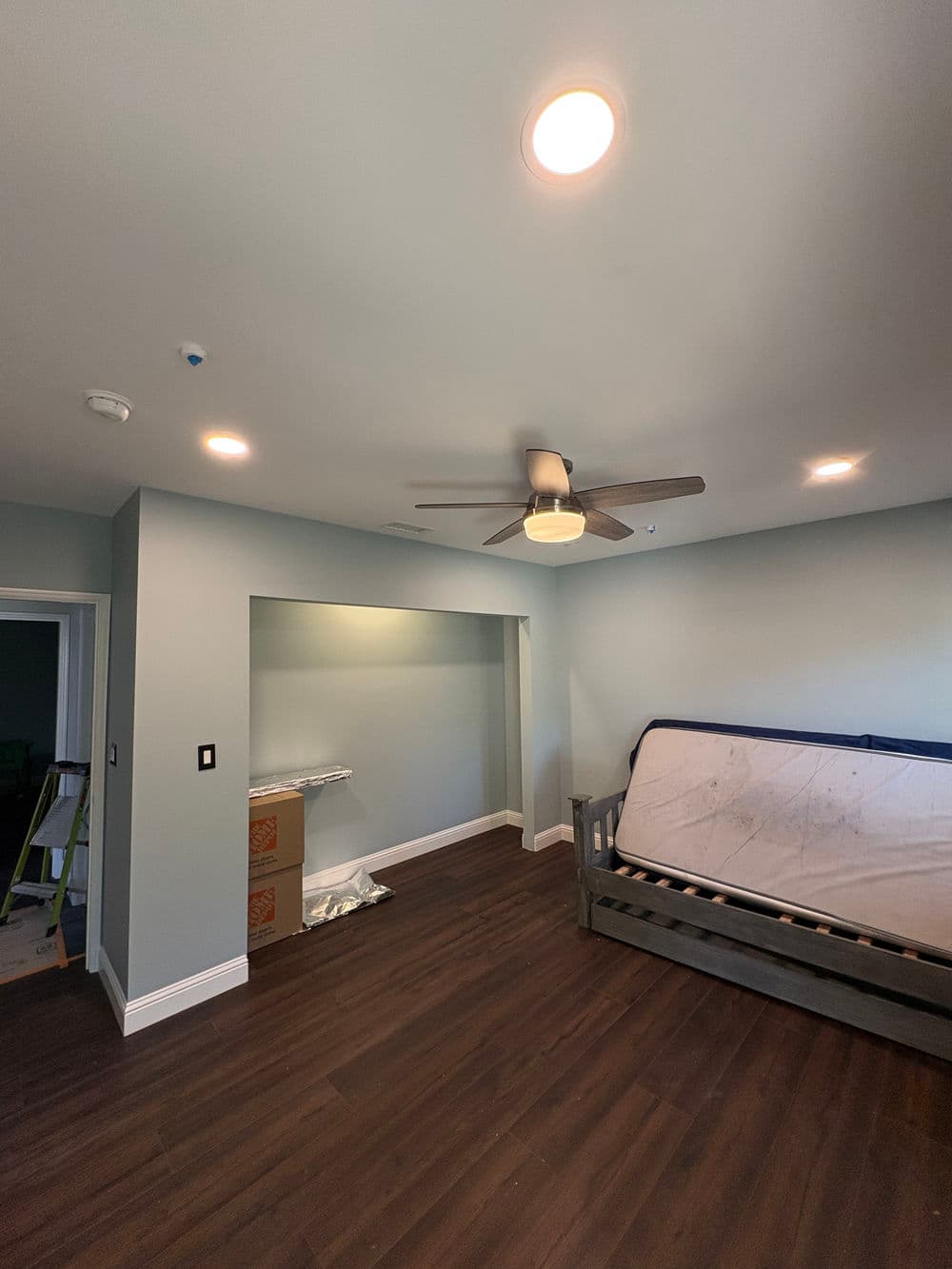 Modern bedroom with light green walls, wooden flooring, and a ceiling fan.