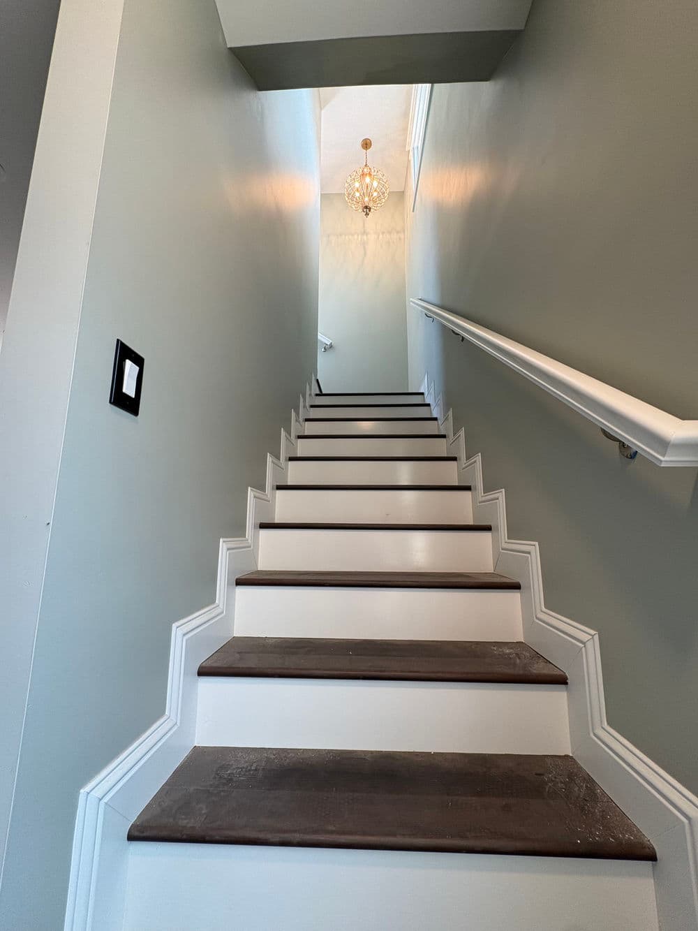 Staircase with white steps and green walls, leading to a chandelier-lit landing above.