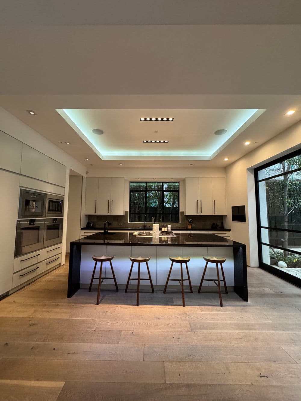 Modern kitchen with sleek black island, bar stools, and natural light filtering through windows.
