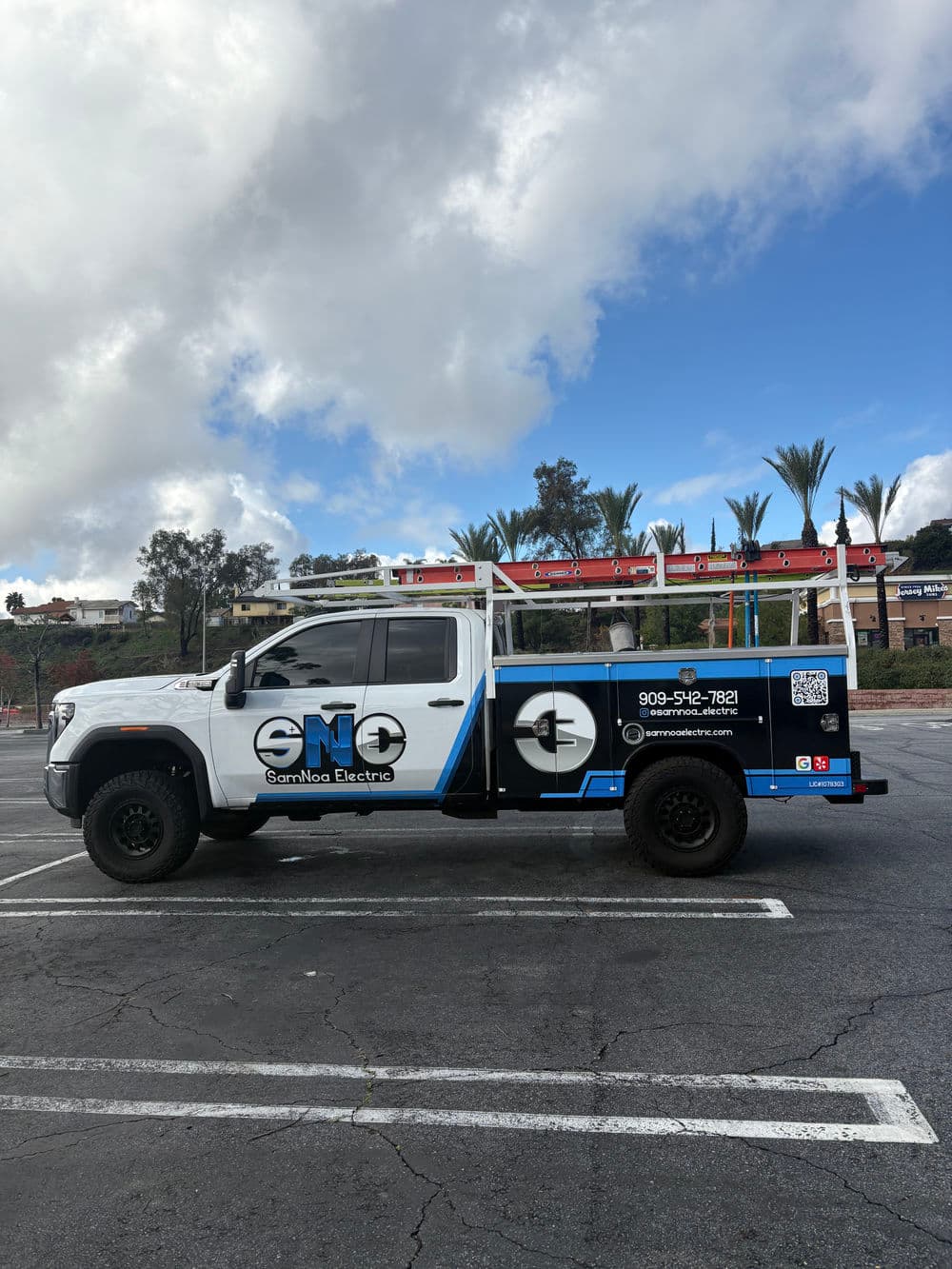 Gambon Electric truck parked in a lot, featuring a blue and white design, logo, and contact info.