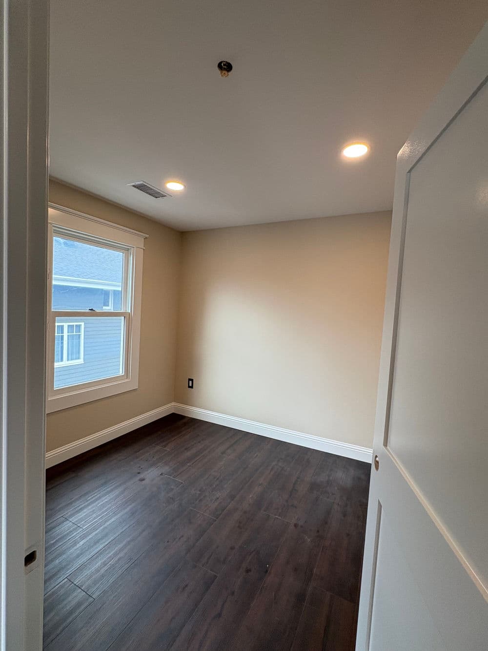 Bright, empty room with wooden floors, white trim, and large window for natural light.